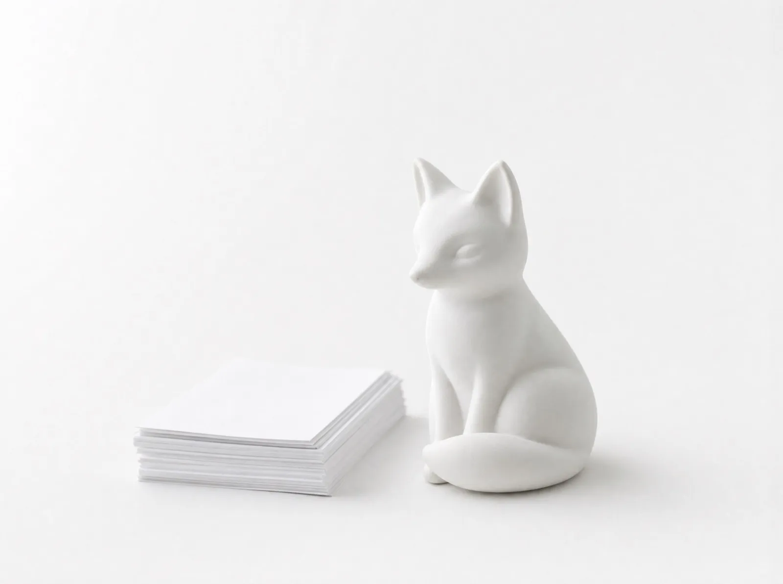 A white ceramic fox figurine sitting beside a neat stack of papers.